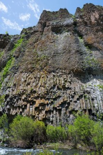 Basalt columns and lush greenery form an impressive cliff landscape on the river under a blue sky,