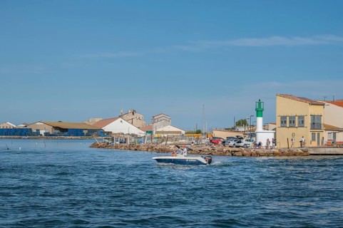 A motorboat with people on board steering it sails in front of the white-green little lighthouse