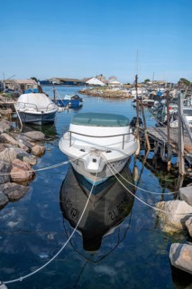 A white moored motor boat with reflection in the calm water of a small harbor of the traditional
