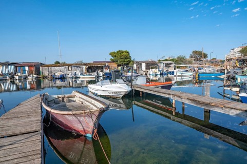 A red-faded fishing boat is moored on a wooden pier in the port of La Pointe Courte, whose