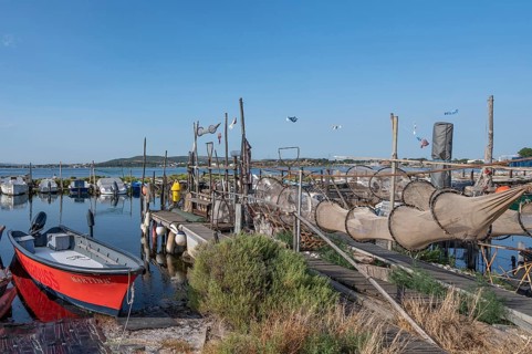 A red fishing boat is lying in the foreground on a wooden pier where numerous fish traps and nets