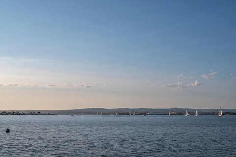 Wide-angle landscape view of Etang de Thau with several sailboats on the water sailing towards the