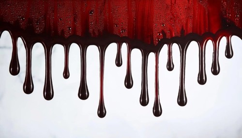 Close-up of dark red liquid dripping down on a white surface, creating a dramatic and eerie effect,