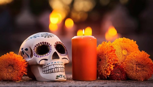 A beautifully decorated Día de Muertos sugar skull is placed beside a burning candle and vibrant