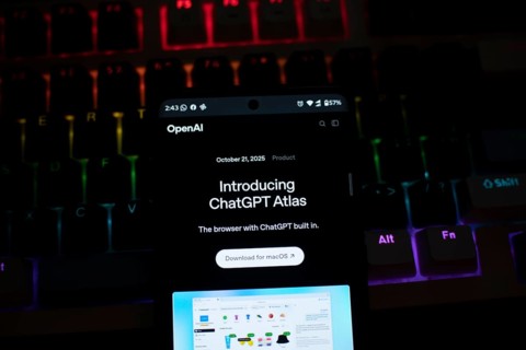 A smartphone displaying ChatGPT Atlas against a colorful, illuminated keyboard