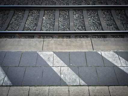 Station tracks with gravel bed, adjacent asphalt and eye-catching strip markings, platform in 27798