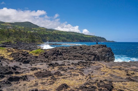 An angler stands on a massive rock of the black lava coast and looks out at the roaring Indian