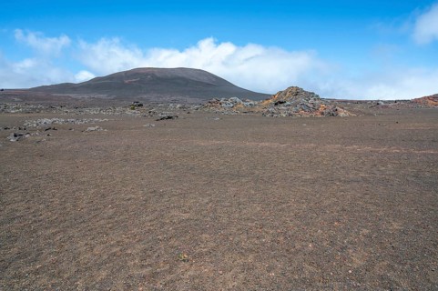 The Route du Volcan crosses the vast, rust-red volcanic desert of the Plaine des Sables, whose