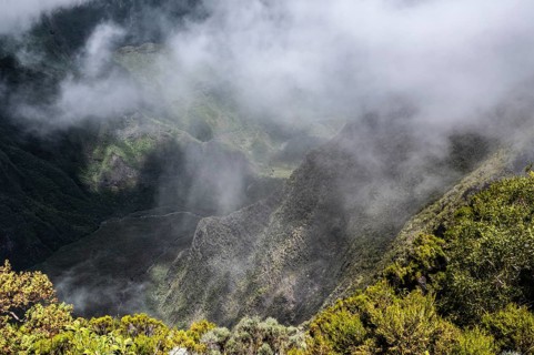 Thick, white clouds of fog cover the steep, green remparts (rock walls) of a caldera of the Piton