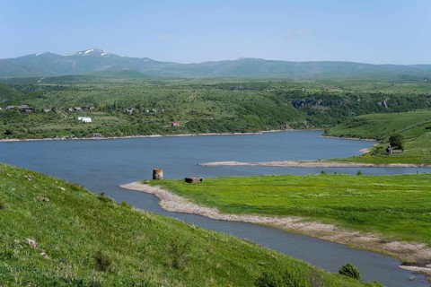 Winding river flows into a lake surrounded by green hills under a blue sky, Kechut Reservoir,
