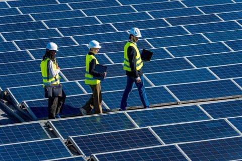Engineers in hard hats and vests walking on a large solar panel array, inspecting the installation
