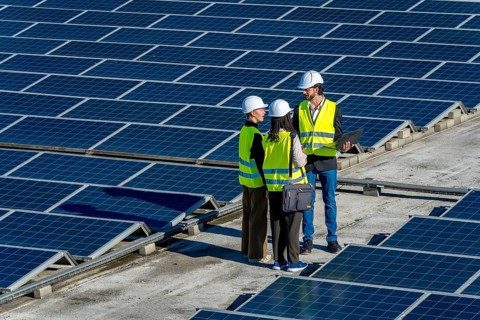 Group of diverse engineers in hard hats and vests working on a solar power station, discussing