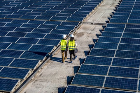 Two engineers, wearing hard hats and safety vests, walking between rows of solar panels on a