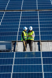 Female engineers wearing hard hats and high visibility vests discussing data on a digital tablet