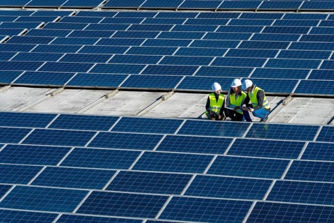 Team of diverse engineers wearing white hard hats and high visibility vests inspecting an array of