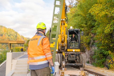 Construction worker with helmet looking at excavator working on rails, autumn environment, signal
