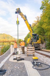 Excavator lifts object on railroad tracks, workers in protective clothing, signal construction at