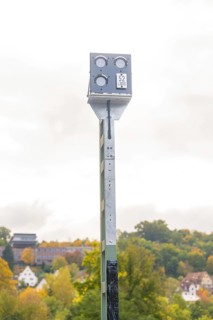 Camera pole in front of autumn landscape with trees and buildings in the distance, Signalbau an der