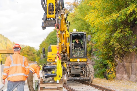 Excavator lifts objects on train tracks, construction workers talking, autumn environment, signal