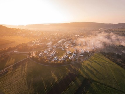 A village surrounded by fields in fog at sunrise with warm orange light, Calw Stammheim, Black