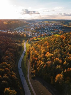 A road snakes through autumn trees towards a small village, Aidlingen, Böblingen district, Germany