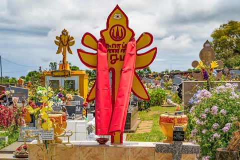 A bright red and yellow Hindu tombstone with religious symbols and a draped cloth stands as a sign
