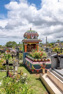 A colorful, richly decorated Hindu shrine with a small temple roof in the cemetery stands between