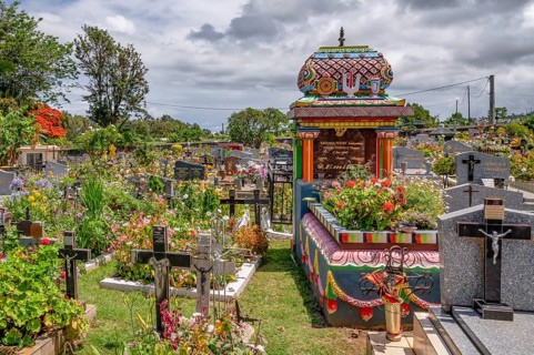 A colorful, richly decorated Hindu shrine with a small temple roof in the cemetery stands between