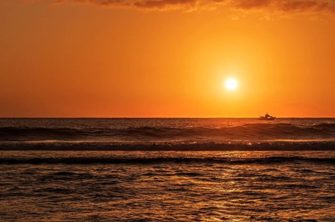 A warm sunset light bathes the sky over the Indian Ocean in orange and gold while a fishing trawler