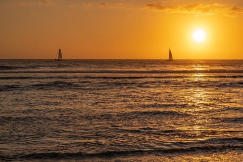 A warm sunset light bathes the sky over the Indian Ocean in orange and gold as two small sailboats