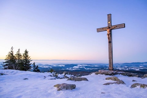 Christian cross on the peak of Mount Lusen with the view over the hills of the bavarian forest at