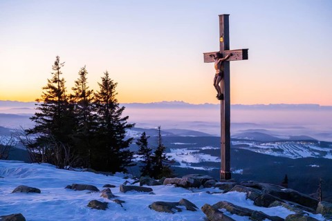 Christian cross on the peak of Mount Lusen with the view over the hills of the bavarian forest at