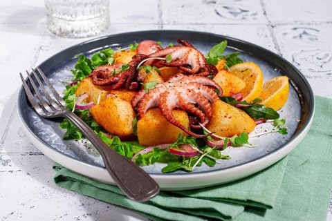 Warm grilled octopus salad with potatoes and fresh herbs, on a stylish plate, homemade