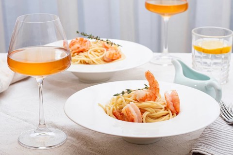 Pasta with shrimp and thyme, served on a white plate, with a glass of white wine, the table is set,