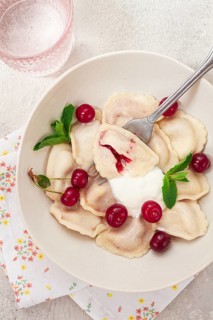 Traditional dumplings with cherries and yogurt, in a bowl, light background, close-up, no people
