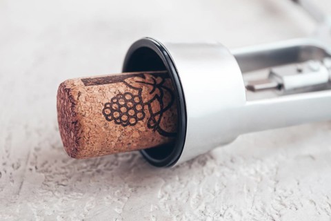 A shiny silver corkscrew rests on a light textured surface, with a wine cork partially inserted,