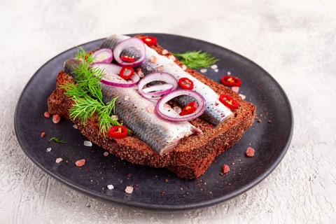 Sandwiches, herring fish, on dark rye bread, sprinkled with onion, chili pepper and herbs, on a
