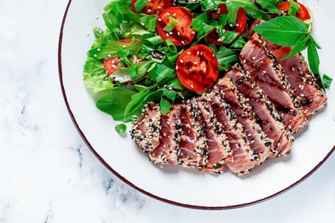 Fried tuna in sesame seeds, sliced on a plate, with fresh salad, on a white plate, homemade