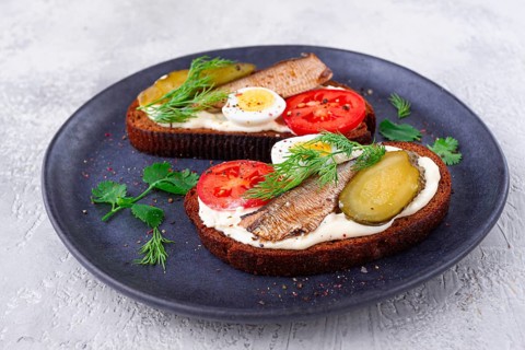 Sandwiches on rye bread with sprats, quail eggs, fresh tomatoes and pickled cucumber, on a dark