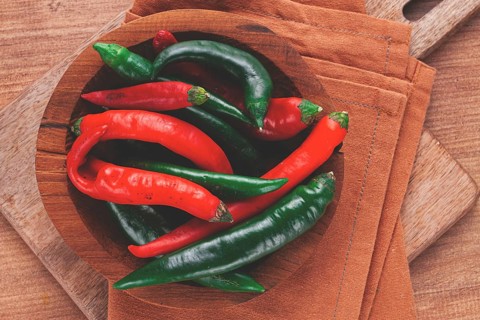 Vibrant red and green chili peppers rest in a wooden bowl, placed on a textured brown cloth atop a