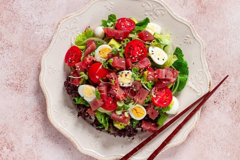 Salad with fresh tuna, cherry tomatoes and quail eggs and avacado, served with chopsticks