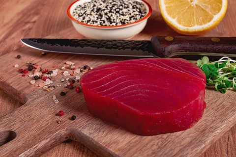 Fresh tuna steak, on a wooden cutting board, with lemon and sesame seeds, on a wooden table