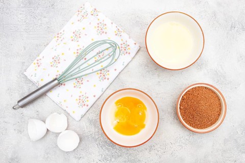 On the dessert preparation table, there are bowls with egg white, and yolk, cane sugar, and a whisk