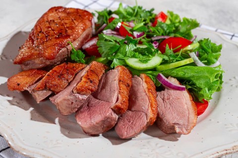 Grilled duck breast is beautifully presented beside a colorful salad of greens, cucumbers,