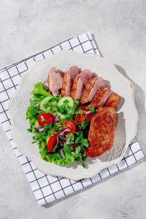 Grilled duck breast is beautifully presented beside a colorful salad of greens, cucumbers,