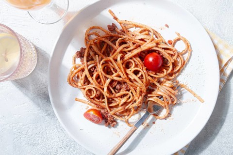 A plate holds freshly cooked spaghetti topped with flavorful meat sauce and garnished with bright