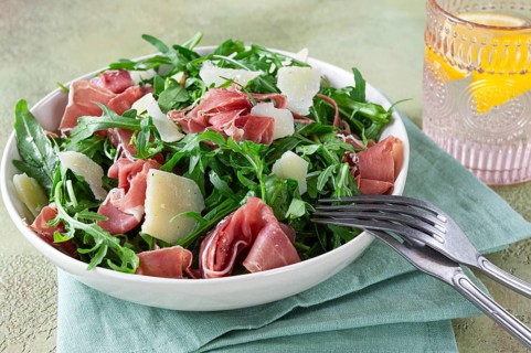 Fresh arugula salad with prosciutto and grated parmesan cheese, on a plate, homemade, no people