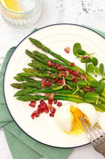 Poached egg with fork, asparagus, bacon slices and herbs, on a white plate, breakfast, close-up, no
