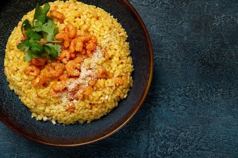 Risotto with shrimp, in a bowl, on a textured surface, with a side dish of fresh coriander,
