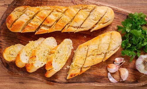 Garlic bread, baguette with garlic butter and herbs, on a wooden board, with herbs and garlic